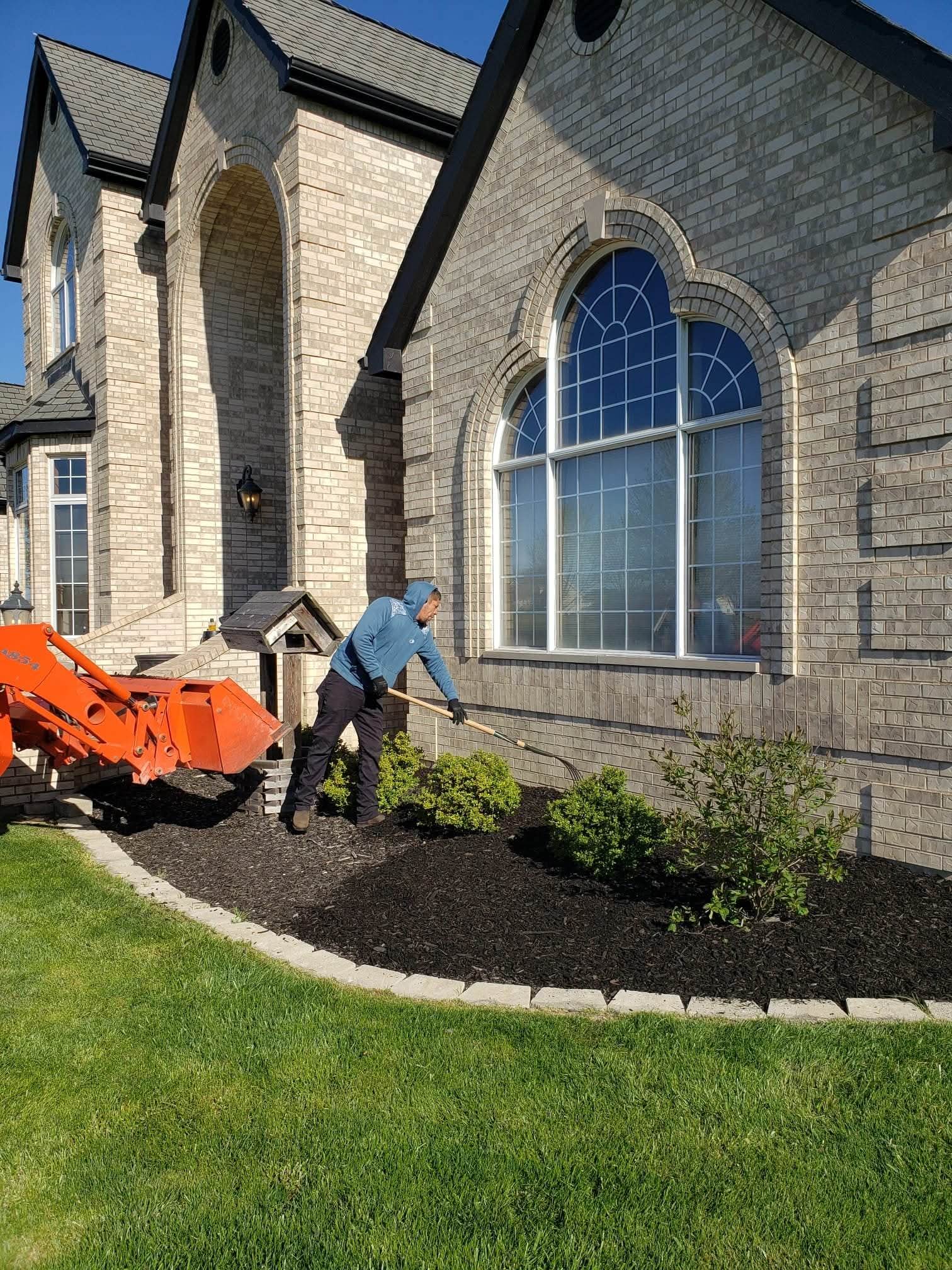 During: the crew raking fresh mulch along a brick house with their orange tractor