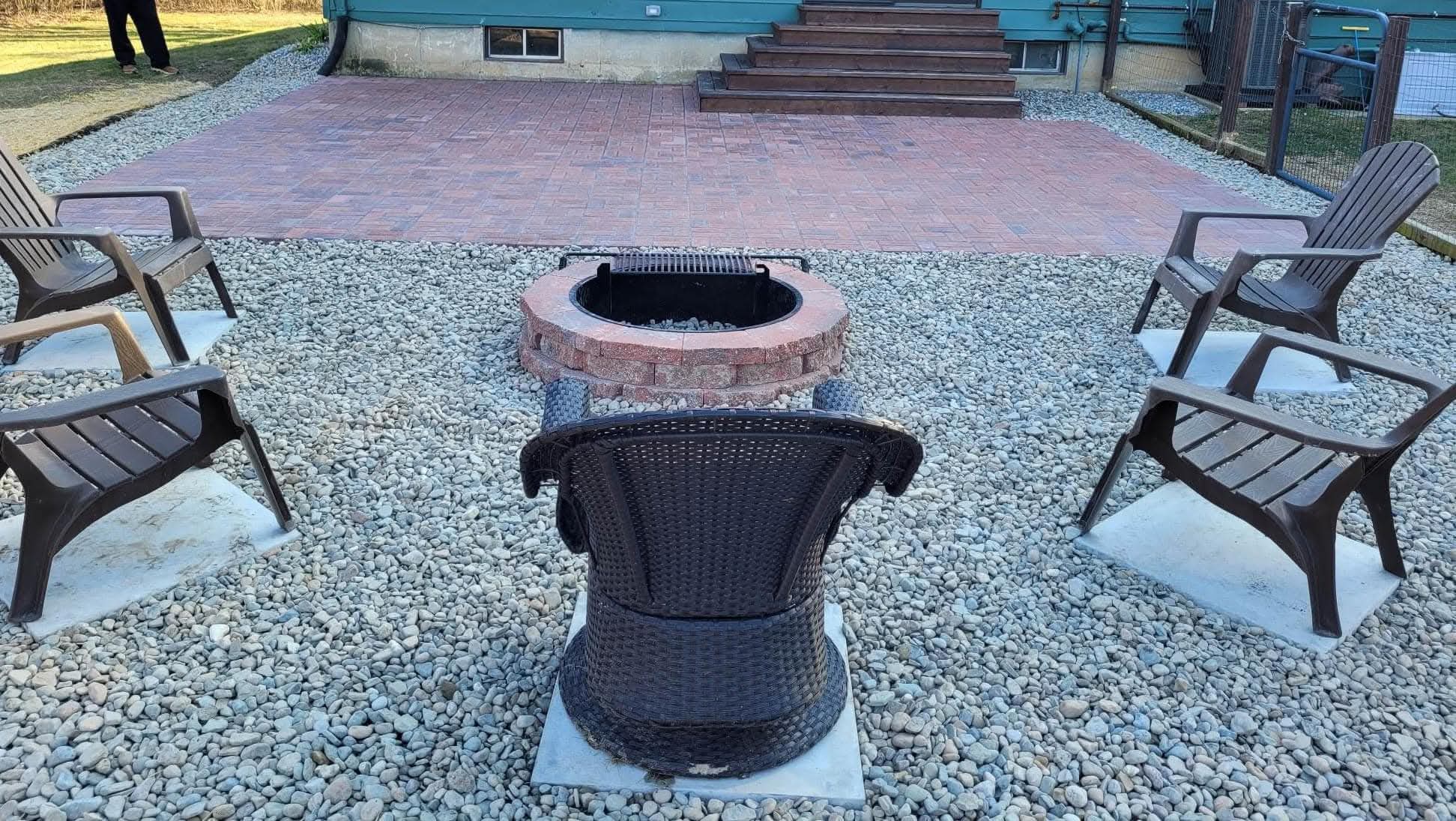 Fire pit circle with chairs on river rock in front of a red paver patio