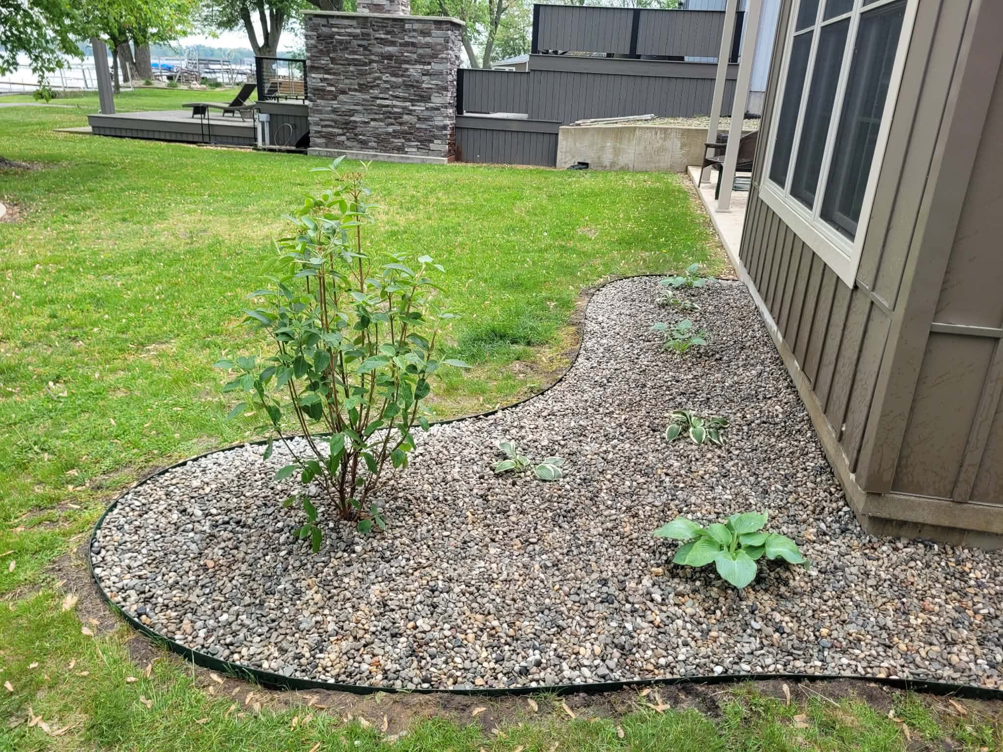 Curved river-rock bed with a shrub and hostas beside a lakeside home