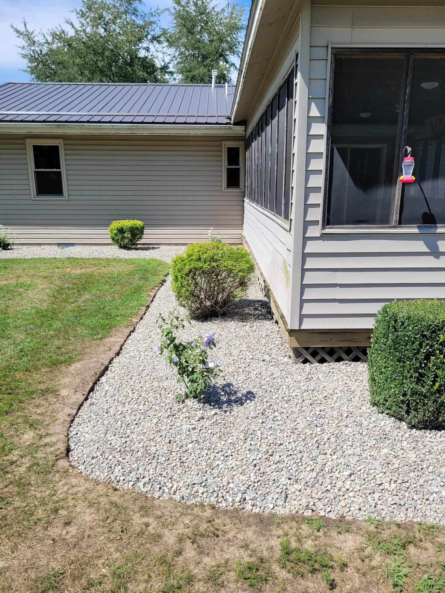 Clean rock bed with trimmed shrubs along a gray house